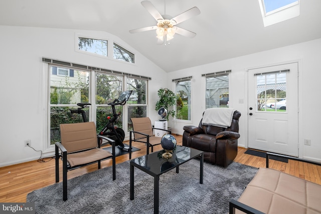 living area with vaulted ceiling with skylight, light wood-type flooring, baseboards, and ceiling fan