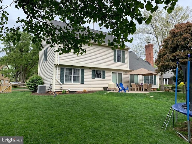 rear view of house featuring a trampoline, central AC unit, a chimney, and a patio