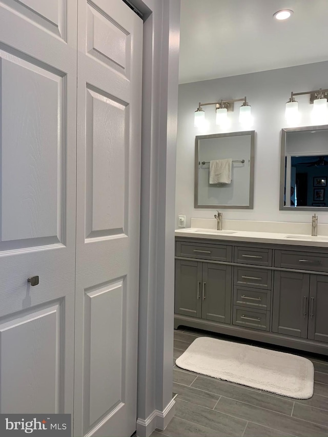 bathroom featuring wood tiled floors, double vanity, recessed lighting, and baseboards