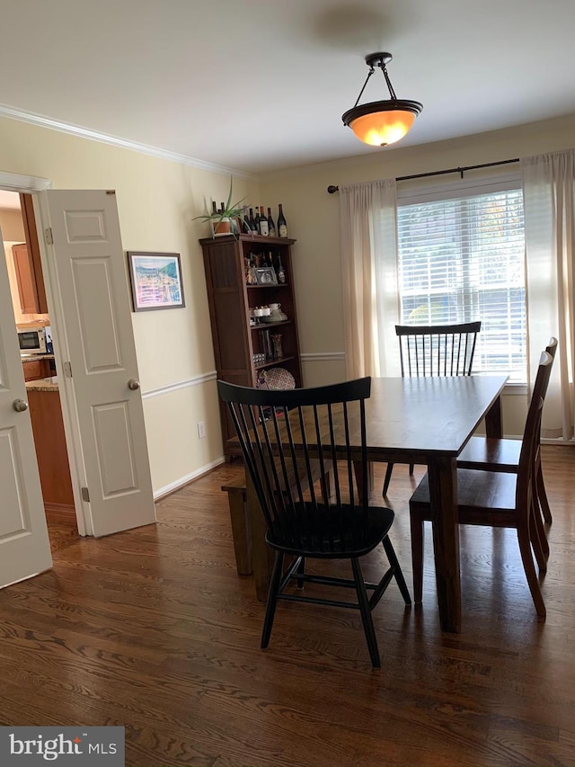 dining space featuring dark wood-type flooring, ornamental molding, and baseboards