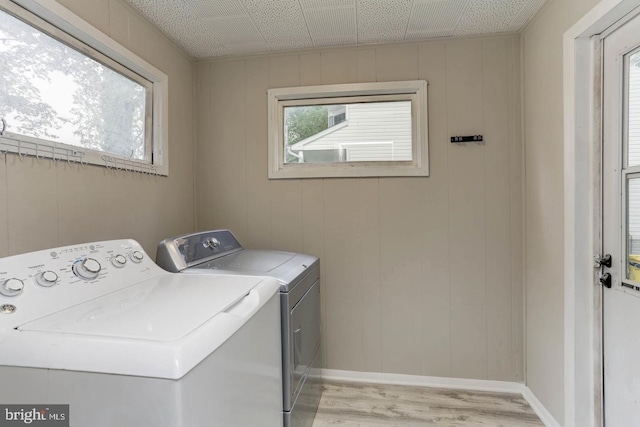 clothes washing area with light hardwood / wood-style floors, washer and dryer, and a wealth of natural light