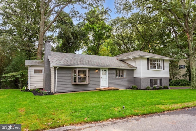 tri-level home with a front yard, roof with shingles, and a chimney