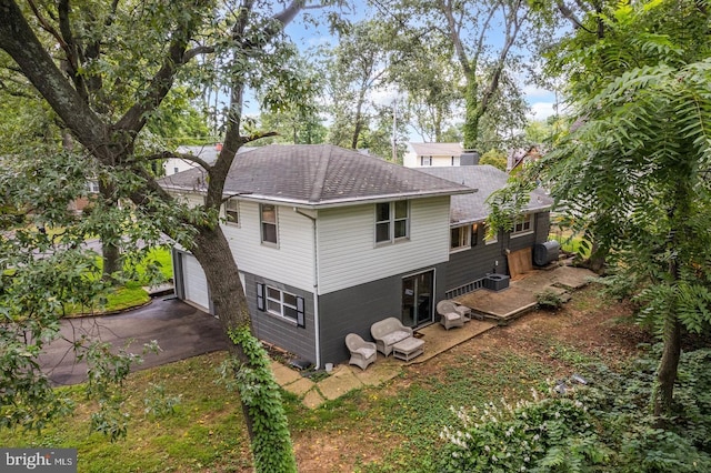 rear view of property featuring driveway, a garage, central AC, and roof with shingles