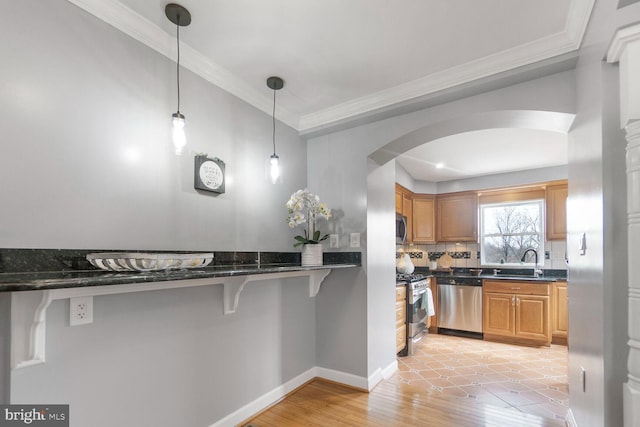 kitchen with arched walkways, pendant lighting, appliances with stainless steel finishes, ornamental molding, and a kitchen bar