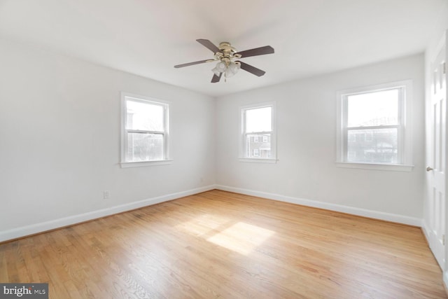 spare room featuring baseboards, light wood-type flooring, a ceiling fan, and a healthy amount of sunlight