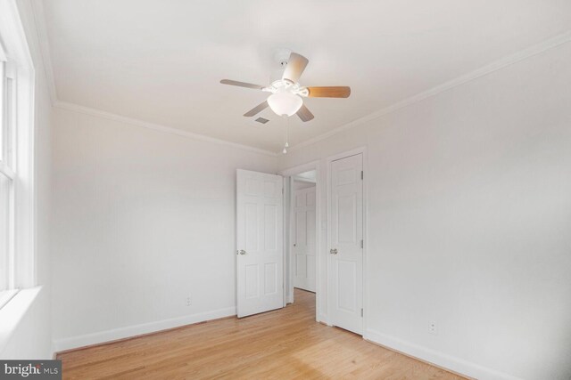 spare room featuring a ceiling fan, light wood-style flooring, baseboards, and crown molding