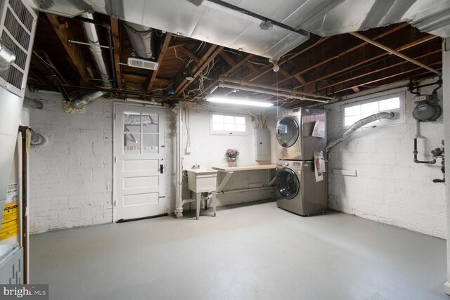 basement featuring stacked washing maching and dryer, a sink, and electric panel