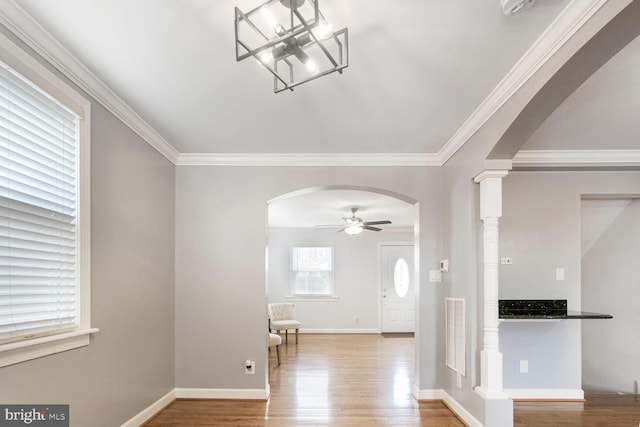 foyer entrance featuring arched walkways, ornamental molding, wood finished floors, and a ceiling fan