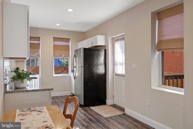 kitchen featuring light stone countertops, dark hardwood / wood-style floors, stainless steel refrigerator, and white cabinets