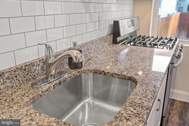 room details with backsplash, sink, stainless steel gas range, and stone counters