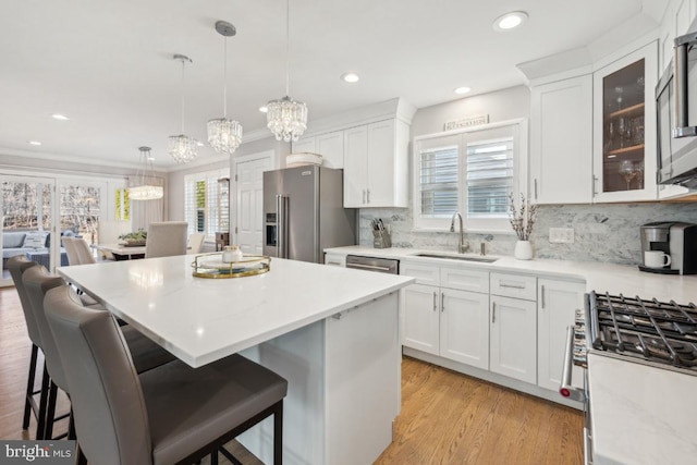 kitchen featuring white cabinets, appliances with stainless steel finishes, glass insert cabinets, hanging light fixtures, and a sink