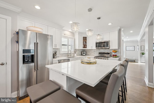 kitchen with a kitchen island, a sink, light countertops, appliances with stainless steel finishes, and glass insert cabinets