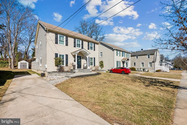 colonial-style house with a storage unit, concrete driveway, a front yard, a residential view, and an outdoor structure