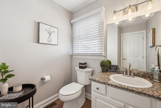 half bathroom with baseboards, visible vents, toilet, wood finished floors, and vanity