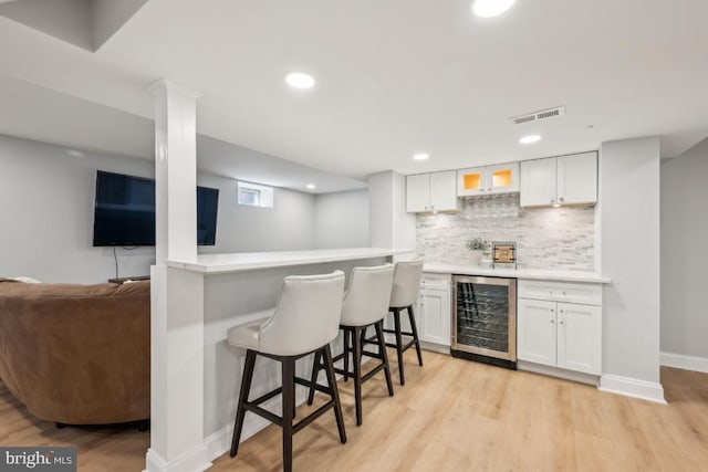 bar featuring light wood-style floors, beverage cooler, visible vents, and a dry bar