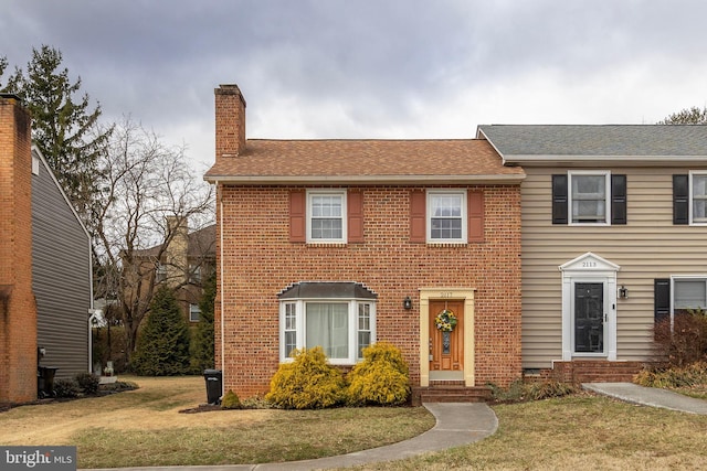 view of front of home featuring a front yard, brick siding, a chimney, and roof with shingles