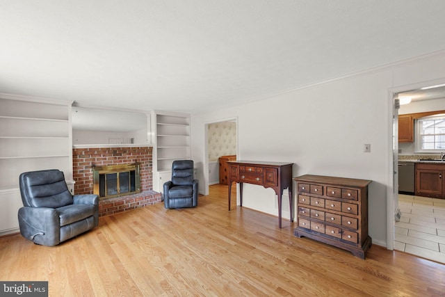 sitting room with built in shelves, a brick fireplace, light wood-style flooring, and crown molding