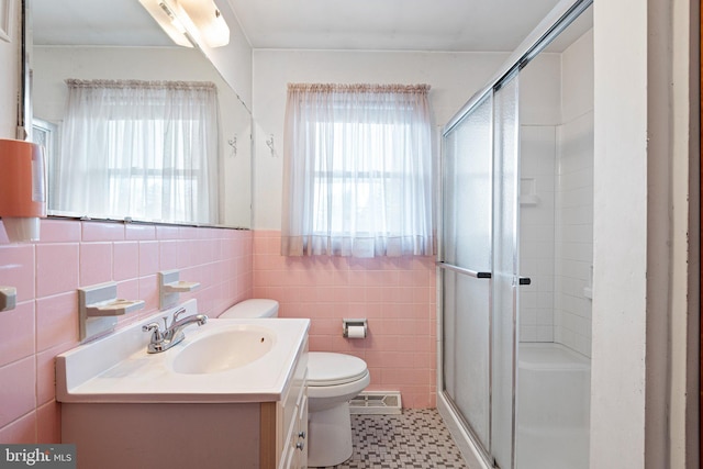 bathroom featuring a shower with door, vanity, a wealth of natural light, and tile walls