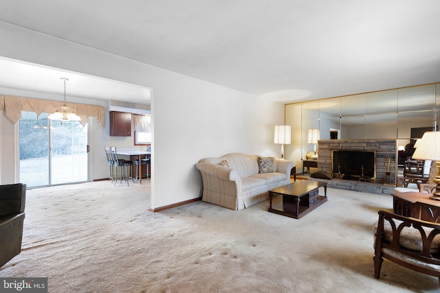 living room with light colored carpet, a stone fireplace, and a chandelier