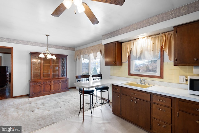 kitchen featuring sink, ceiling fan with notable chandelier, tasteful backsplash, light carpet, and decorative light fixtures