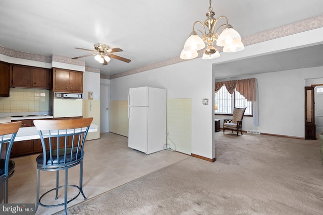 kitchen featuring light carpet, dark brown cabinets, white appliances, ceiling fan with notable chandelier, and backsplash