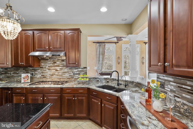 kitchen featuring sink, backsplash, light stone countertops, stainless steel gas stovetop, and ornate columns