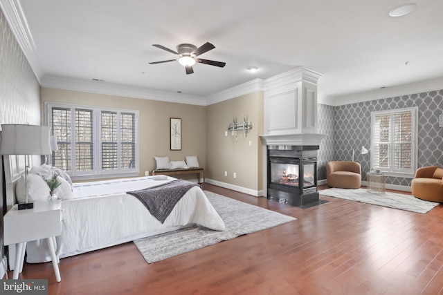 bedroom with ceiling fan, a multi sided fireplace, ornamental molding, and dark hardwood / wood-style flooring