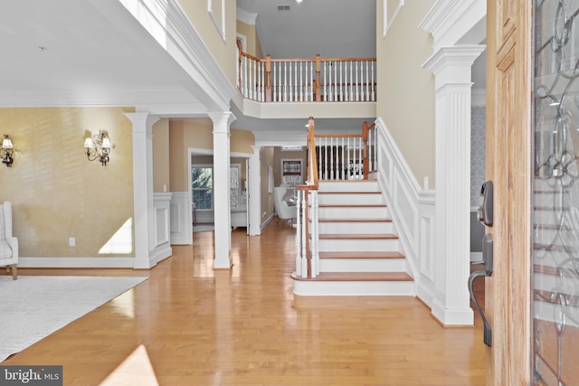 entrance foyer featuring a towering ceiling, ornamental molding, decorative columns, and light wood-type flooring