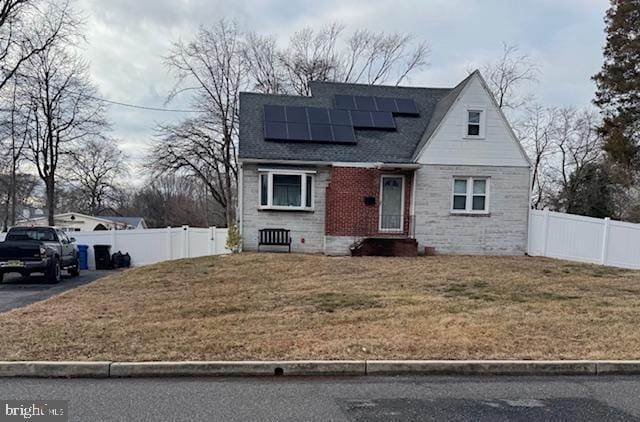 view of front facade featuring fence, a front lawn, solar panels, and roof with shingles