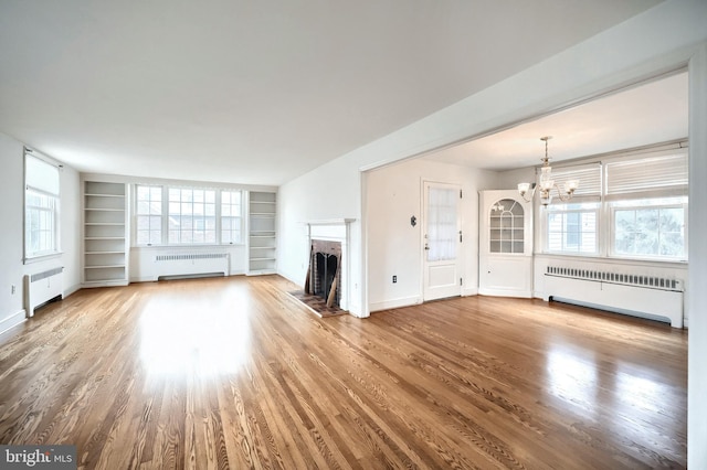 unfurnished living room with hardwood / wood-style flooring, radiator heating unit, and a chandelier