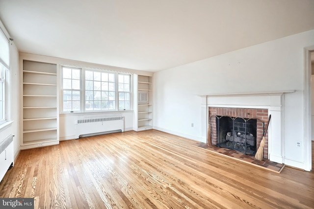 unfurnished living room featuring radiator heating unit, a fireplace, hardwood / wood-style floors, and built in features