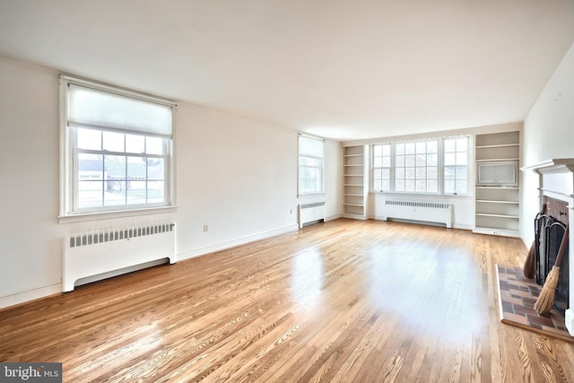 unfurnished living room with radiator heating unit, a fireplace, and light wood-type flooring