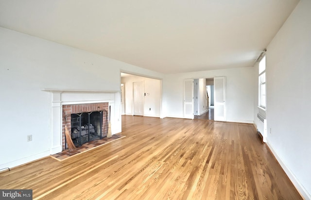 unfurnished living room with wood-type flooring, a brick fireplace, and radiator