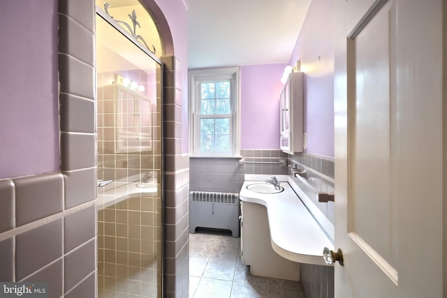 bathroom with tile patterned floors, tile walls, radiator heating unit, vanity, and a shower with door