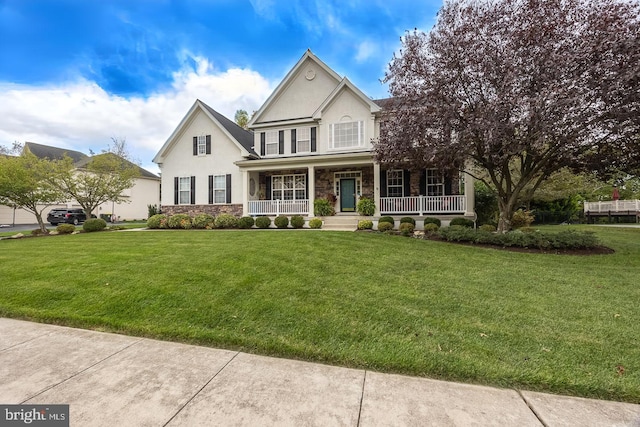 view of front of home with stone siding, a front yard, covered porch, and stucco siding