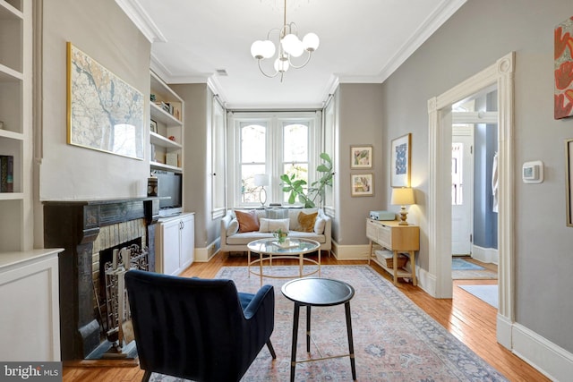 living area featuring a notable chandelier, ornamental molding, a fireplace, and light wood finished floors