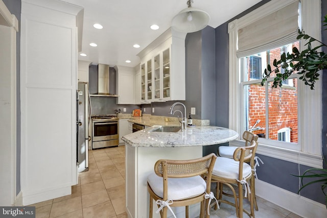 kitchen with a sink, white cabinetry, a peninsula, appliances with stainless steel finishes, and wall chimney exhaust hood