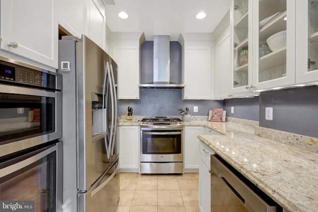 kitchen featuring wall chimney range hood, light tile patterned floors, white cabinets, and appliances with stainless steel finishes