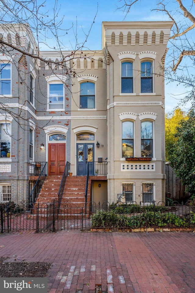 view of front facade with french doors, brick siding, and a fenced front yard