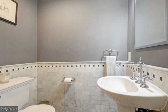 bathroom featuring a sink, toilet, tile walls, and wainscoting