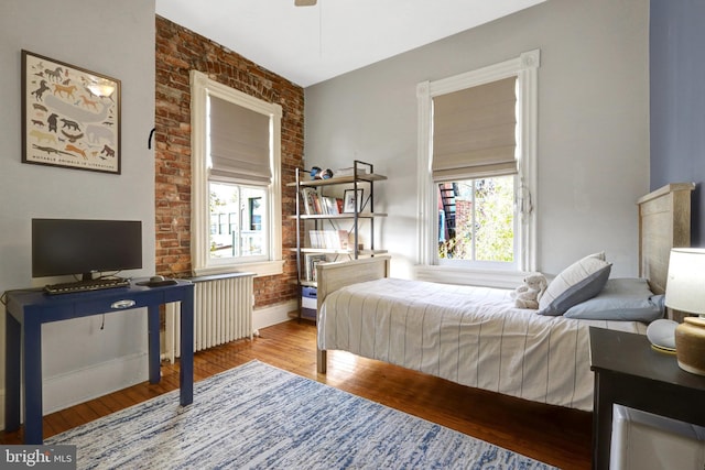 bedroom featuring radiator, brick wall, baseboards, and wood finished floors