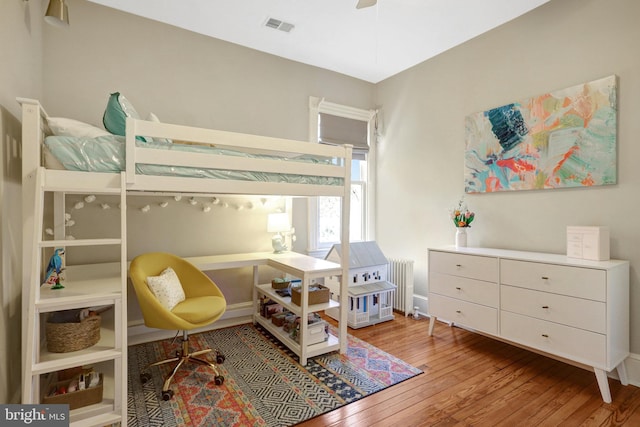 bedroom with hardwood / wood-style floors, radiator heating unit, and visible vents