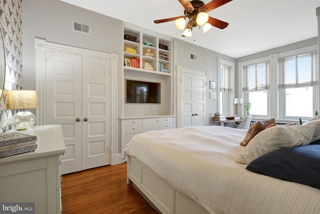 bedroom featuring ceiling fan, visible vents, multiple closets, and light wood-style flooring