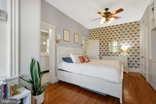 bedroom with baseboards, hardwood / wood-style flooring, ensuite bathroom, and wallpapered walls