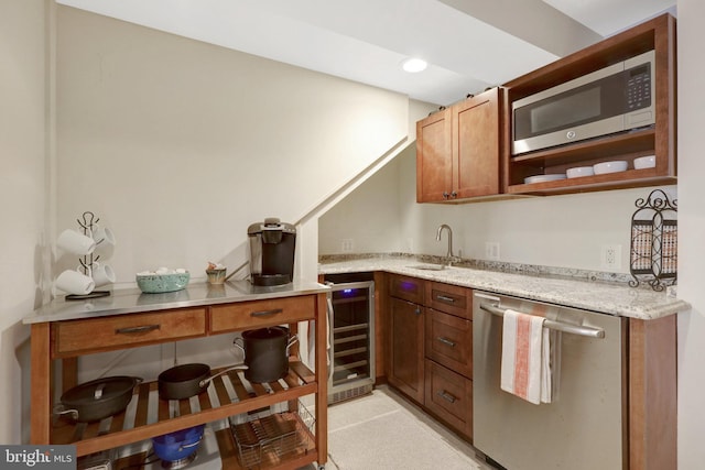 kitchen with beverage cooler, appliances with stainless steel finishes, light stone counters, and a sink