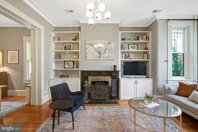 living room featuring visible vents, built in shelves, crown molding, a fireplace with flush hearth, and wood finished floors