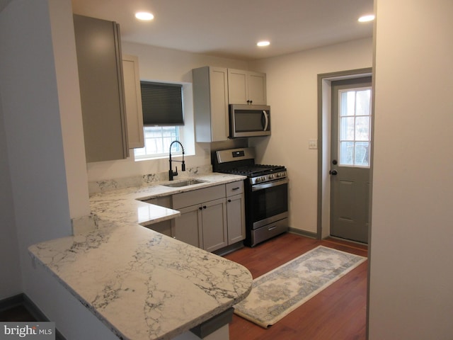 kitchen featuring sink, light stone counters, dark hardwood / wood-style flooring, kitchen peninsula, and stainless steel appliances