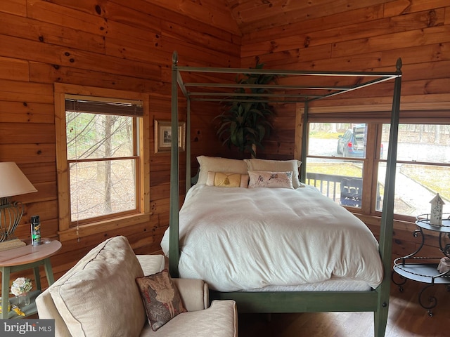 bedroom with vaulted ceiling, wood walls, and wood finished floors