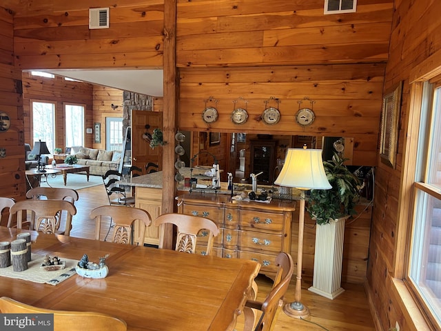 dining area featuring light wood finished floors, wood walls, and visible vents