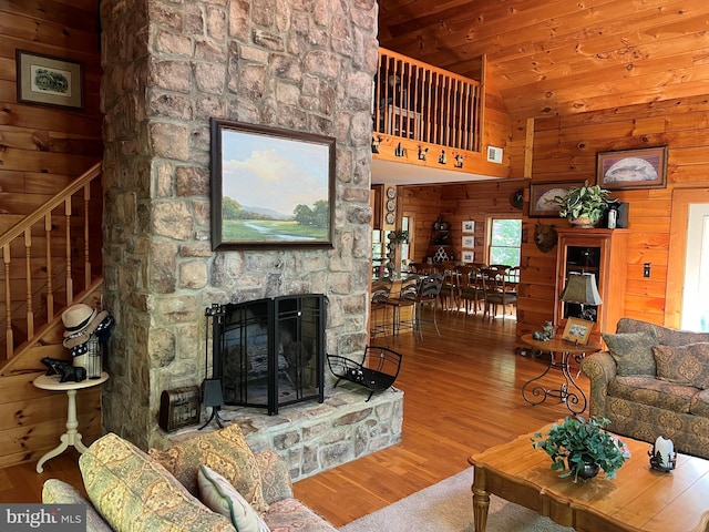 living area featuring a stone fireplace, wooden walls, wood finished floors, wood ceiling, and stairway